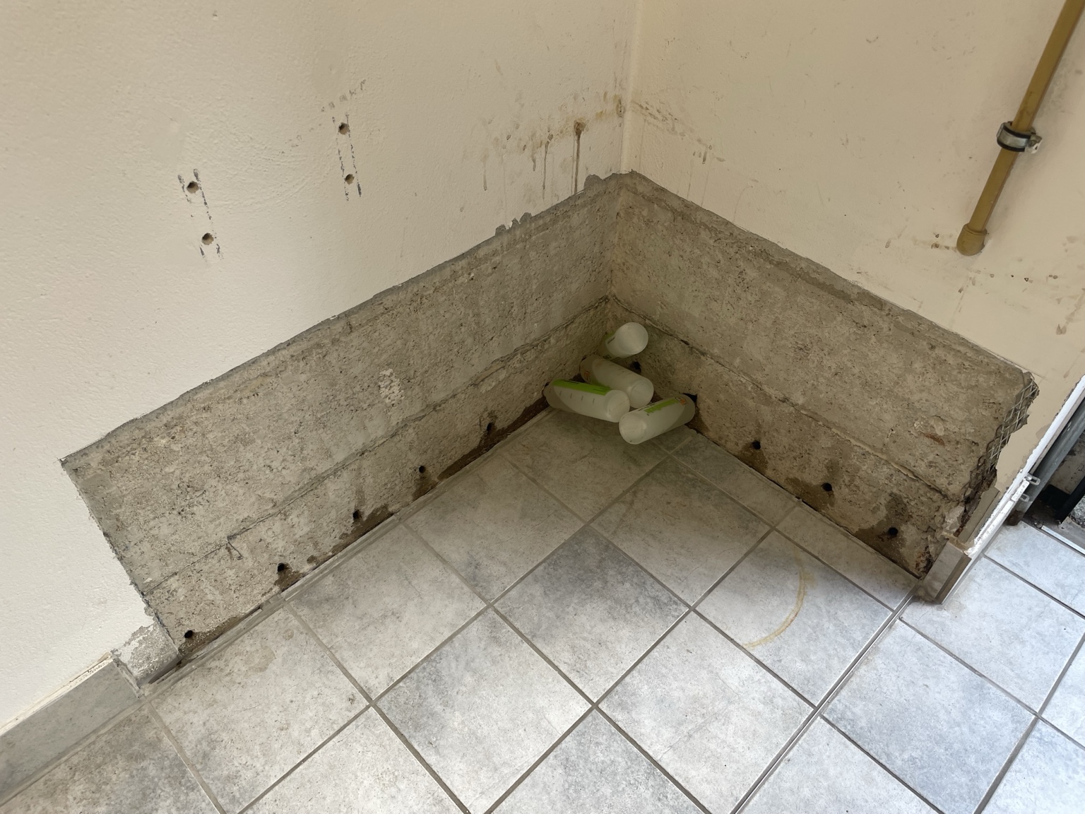 Vorher: freigelegter Sockelbereich in einer Raumecke mit gefliestem Boden